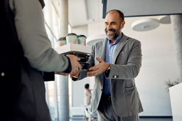 Happy businessman receiving take-away food from delivery man while being at work