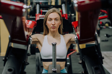 Woman shakes her legs over the bar. Girl fitness instructor is engaged on the simulator in the gym.