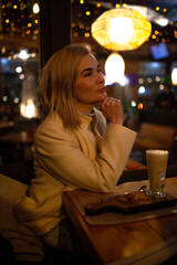 Beautiful woman sit in night cafe and eat fast cafe and dink coffee in evening.