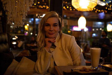 Beautiful woman sit in night cafe and eat fast cafe and dink coffee in evening.
