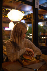 Beautiful woman sit in night cafe and eat fast cafe and dink coffee in evening.