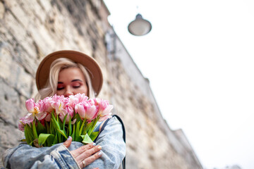 Fashion style woman dressed jeans jacket, hat and red dress walking in the street of old city with bouquet of flowers