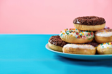Donut worry, be happy. Cropped shot of various colourful round glazed donuts with sprinkles on the plate over blue and pink background