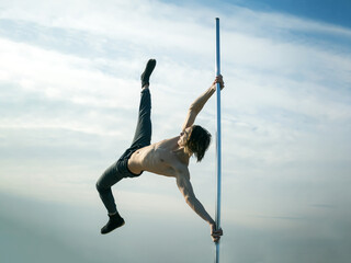 Young strong man pole dancing. Pole dance sport. pole dance training of young man dancer on blue...