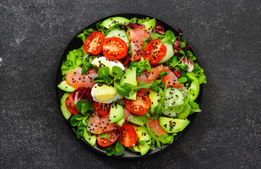 Keto diet salad with salted salmon, avocado, egg, sesame seeds, olive oil, tomatoes and mixed herbs. Black background, top view, copy space