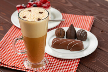 Cup of coffee and saucer with chocolate sweets on wooden table