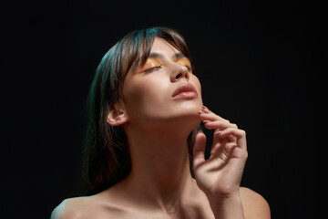 Sensuous young brunette woman with professional makeup touching her face, posing with eyes closed...