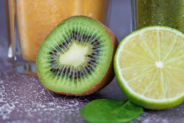 Fototapeta na wymiar A close-up of lime and kiwi fruit halves in front of glasses of orange juice