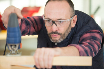 Obraz premium man using electric jigsaw to cut pine timber