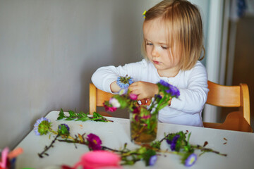 Adorable toddler girl making flower bouquet at home