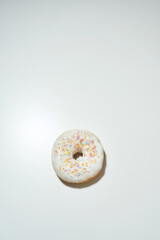 Too much sugar. Vertical shot delicious donut with colorful sprinkles and white sugar glaze isolated on light background, copy space for text