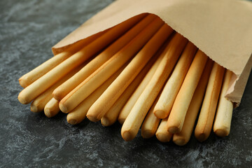 Paper bag with grissini breadsticks on black smoky background