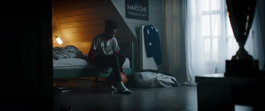 WIDE Bored African American Black kid teenager boy playing with basketball in his attic bedroom at home. Shot with 2x anamorphic lens