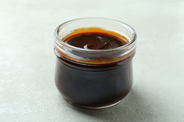 Glass jar of barbecue sauce on white textured background