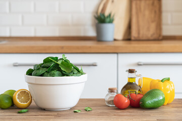 Bowl of fresh green spinach on the kitchen table. Modern kitchen interior in the background