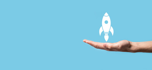 Male hand holding rocket icon that takes off, launch on blue background. rocket is launching and...