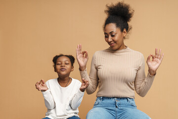 Smiling black mother and daughter gesturing while meditating together