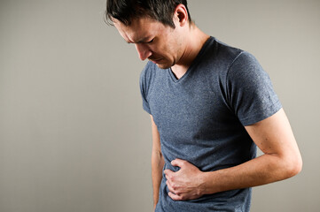 Man in pain holding his hurting stomach isolated on the gray background. Abdominal pain.