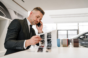Mature man talking on cellphone while choosing car in showroom