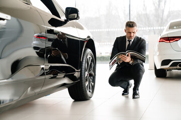 Mature white man choosing and examining car in showroom