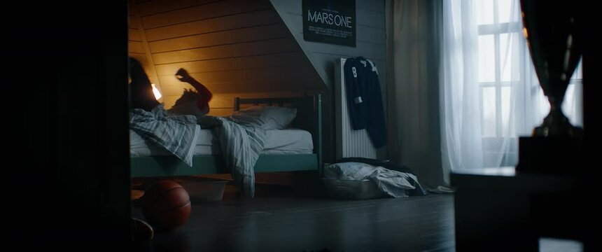 WIDE Bored African American Black kid teenager boy playing with basketball in his attic bedroom at home. Shot with 2x anamorphic lens