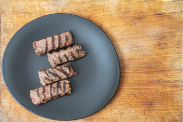 Traditional Romanian grilled minced meat, mici or mititei on a black ceramic plate and a wood board 