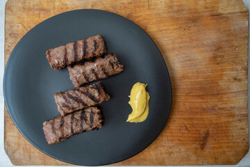 Traditional Romanian grilled minced meat, mici or mititei on a black ceramic plate with mustard
