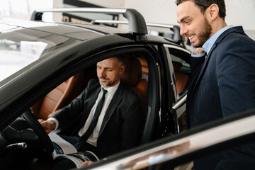 Fototapeta na wymiar Mid pleased manager showing car to mature customer in showroom