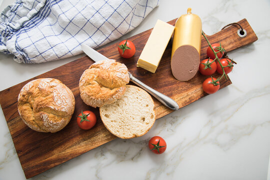 Feine Leberwurst aus Kalb und Schwein mit Weizen Rosen Br&ouml;tchen, Tomaten, Butter und Messer auf Holzbrett, Geschirrtuch und Marmor Hintergrund als Fr&uuml;hst&uuml;ck