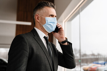 White businessman in face mask talking on cellphone at office
