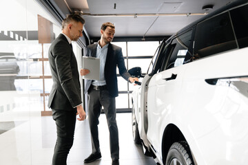 Mid pleased manager showing car to mature customer in showroom