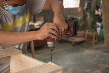 Close-up of carpenter using electric drill in workshop and routing out holes Cabinetmaker drilling wood on table. Joinery work on the production and renovation of wooden furniture. Small Business