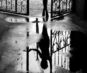 Silhouette of a girl standing in the street. Creative photo of rain mood. Woman's reflection on a wet pavement after the rain. The legs of a woman, black and white background.