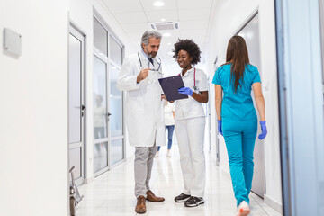 Man and woman doctor having a discussion in hospital hallway while holding digital tablet. Doctor...