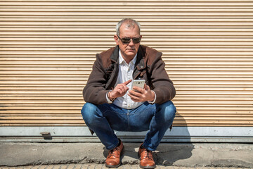 adult man squatting using mobile phone in the city