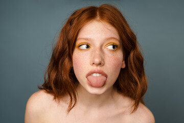 Shirtless ginger woman showing her tongue and looking aside