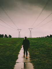 A girl with yellow boots walking on a rainy day on a path near power lines