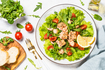 Green salad with baked fish at white table.