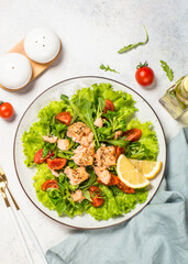 Green salad with baked fish at white table.