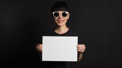 Female or woman hands is holding blank A4 white paper on black background.she wear black t shirt and Sunglasses