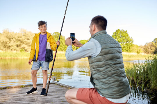 father photographing son with fishing rod on river
