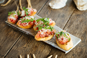Salmon bruschettas with grated cheese and arugula on the wooden background