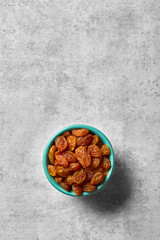 Raisins in a bowl viewed from above on a grey background. Top view. Copy space