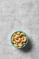 Cashew nuts in a bowl viewed from above on a grey background. Top view. Copy space