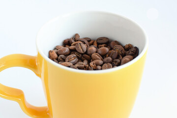 Yellow ceramic cup filled with roasted coffee beans. Selective focus.