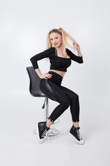 Beautiful blonde in black clothes and a black chair on a white background. 