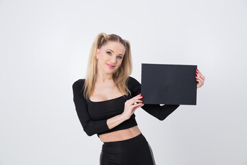 A beautiful blonde in black clothes holds a sheet of black paper in her hands. 