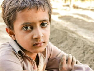 closeup of a poor staring hungry orphan boy in a refugee camp with sad expression on his face and his face and clothes are dirty and his eyes are full of pain