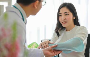 Fototapeta premium Doctor helping Asian patient with arm sling