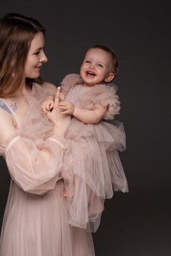 Woman in light clothes have fun with cute child baby girl. Mother, little kid daughter isolated on grey wall background, studio portrait. Mother's Day love family, parenthood childhood concept